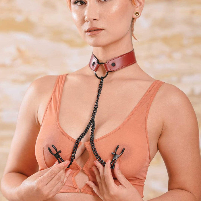 A woman in a peach-colored top and a Sportsheets Saffron Collar with Nipple Clamps poses confidently with a chain accessory.