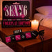 A candle-lit bedside table features the Sexy 6 Dice Game for Couples - Foreplay Edition and a pouch with six pink and black dice, setting a romantic and intimate mood.