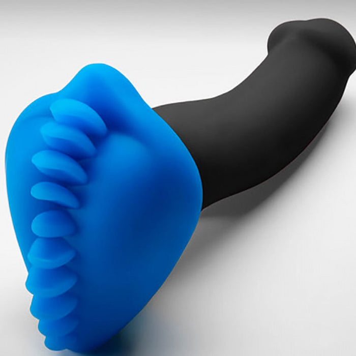 The Shagger Extreme Textured Dildo Base for Harness Play by Bumpher by Bananapants features a striking two-toned design in black and azure blue. The black portion of this silicone sex toy is cylindrical, while the azure blue end boasts textured ridges that resemble teeth or spikes, creating a visually and tactilely intriguing contrast. Presented on a white, smooth surface, this manual stimulator offers an appeal that is both sensual and eye-catching.