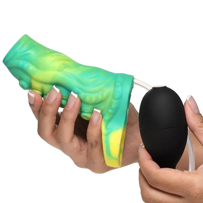 A person holds the Siphon Green Tentacle Squirting Penis Enhancer, featuring a vibrant blend of green, yellow, and blue textures, in one hand while squeezing the attached black bulb pump with the other.