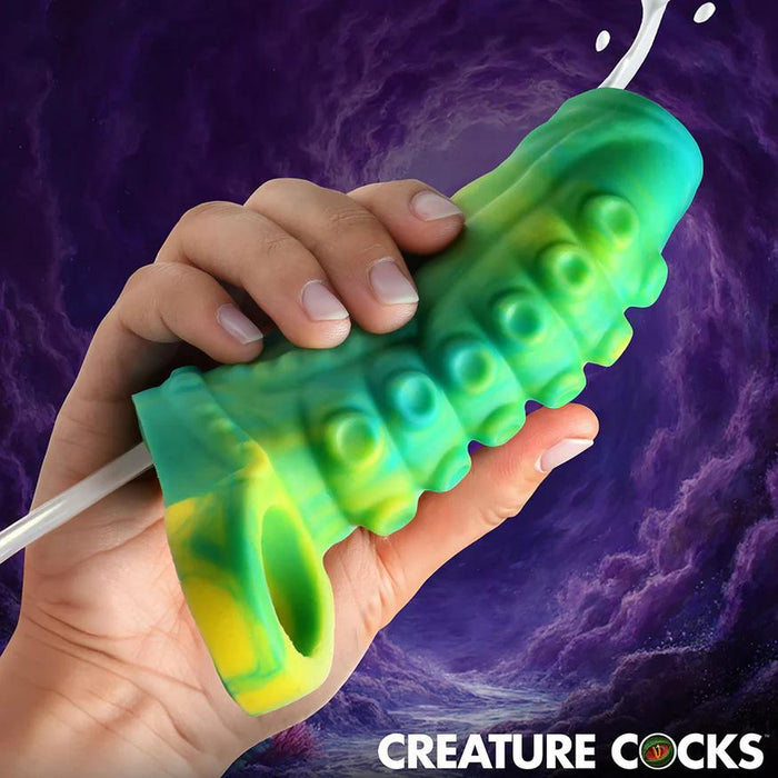 A hand holds the Siphon Green Tentacle Squirting Penis Enhancer, featuring a green and yellow bumpy texture with a hole at the tip spraying liquid. A swirling purple vortex is behind, with "CREATURE COCKS" in the bottom right corner.