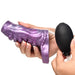 A person holds the Siphon Tentacle Squirting Purple Penis Enhancer in one hand and squeezes the attached black inflation bulb with the other.
