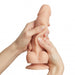Two hands hold the Sliding Skin Realistic XX-Large 8.25 Inch Vanilla Silicone Dildo with Suction Cup by Lovely Planet. The silicone dildo, which is flesh-colored and realistic in appearance, bends slightly as it is being squeezed. The background is white and devoid of any additional details or objects.