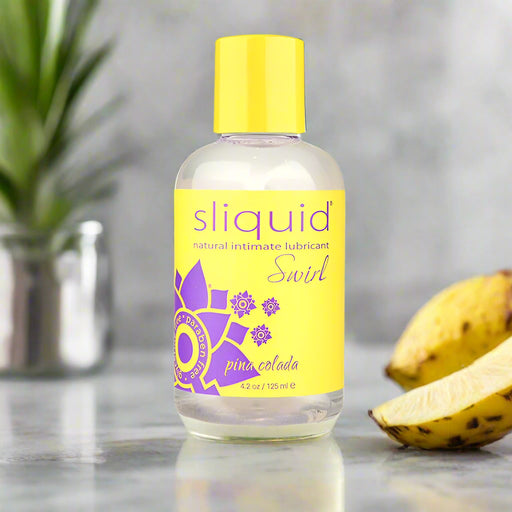 A bottle of Sliquid Swirl Pina Colada Flavored Lubricant with a Piña Colada flavor. The clear 4.2-ounce, vegan-friendly, water-based lube features a yellow label adorned with purple floral graphics and text, along with a matching yellow cap. The label reads "natural intimate lubricant" and states the volume as 125 ml.