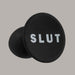A black phone grip with the word "SLUT" in white capital letters on the round top, designed to match your bold style just like the Slut Silicone Butt Plug by Blush, made from premium platinum-cured silicone.