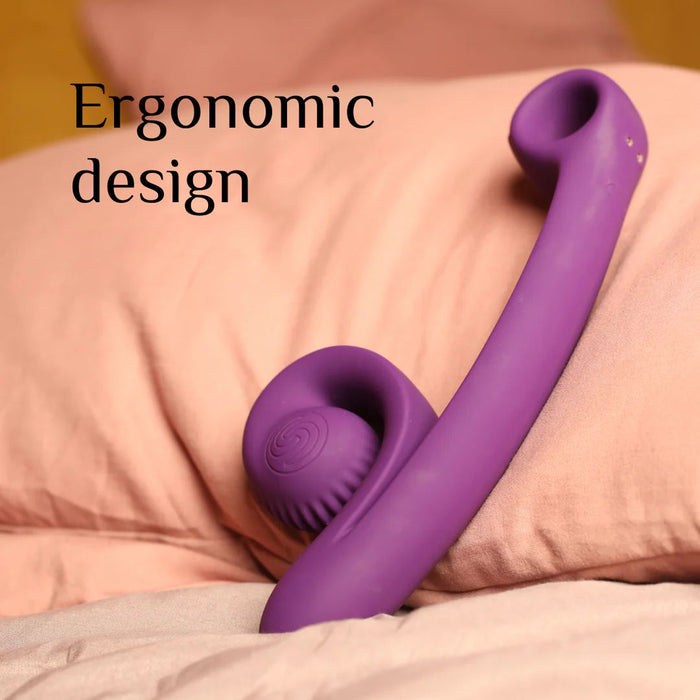 A purple Snail Vibe Curve Ultra Powerful 2 Motor Dual Stimulating Vibrator by Snail Vibe rests on a bed with pink sheets. The waterproof vibrator features an ergonomic curved handle and two head attachments, perfect for g-spot stimulation. Text in the top left corner reads "Ergonomic design.