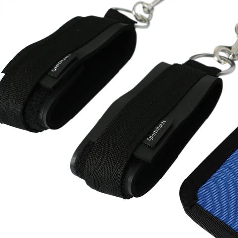 Two black sports ankle straps with metal D-rings and Velcro closures are shown on a white background. The adjustable restraints are connected to a blue harness pad. The brand name "Sportsheets" is visible on one of the sports cuffs, which are part of the Sportsheet The Original Bed Bondage Sheet - King Size set.