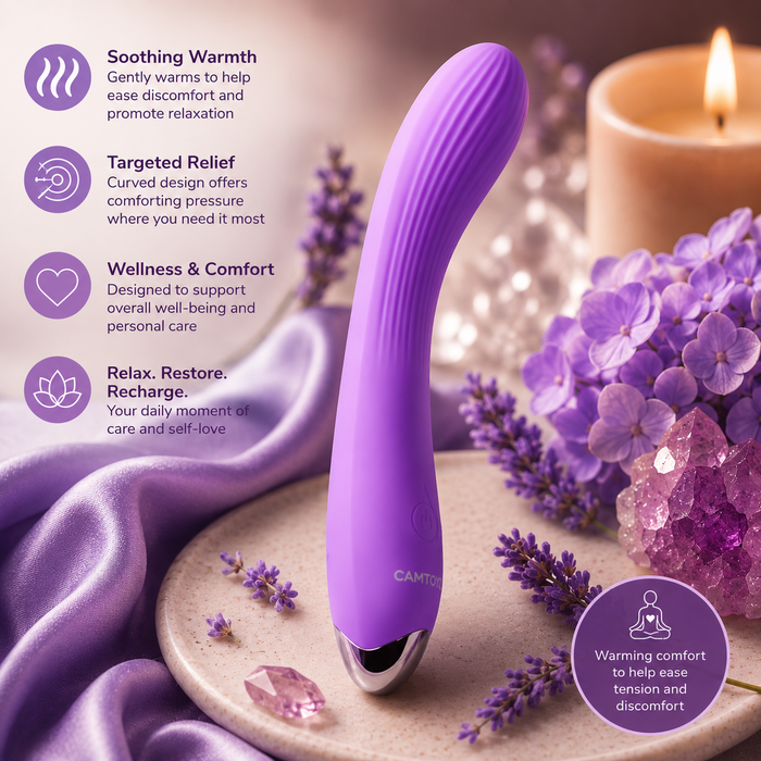 The Kian Slim Ergonomic Warming Silicone Vibrator lies on silky purple fabric among lavender, hydrangeas, a lit candle, and stones. Informational text highlights soothing warmth, targeted relief, wellness, and relaxation benefits.