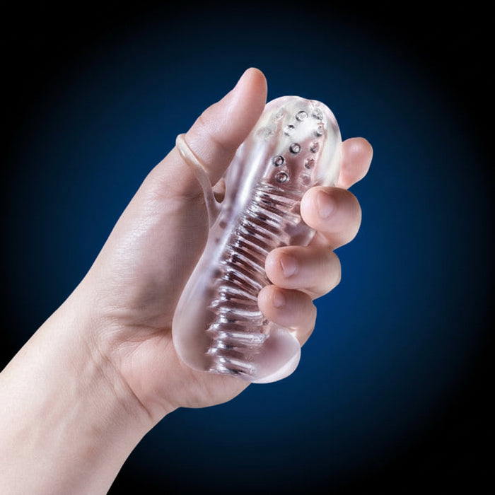 A hand squeezes the Rize Squeezy See Through Textured Compact Stroker with Loop Grip—a transparent, flexible stroker with internal bumps and an ergonomic loop grip—against a dark blue background.