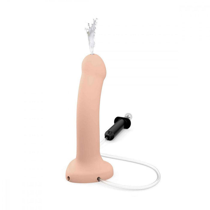The Strap-On-Me 5.7 Inch Silicone Squirting Cum Dildo - Vanilla by Lovely Planet features a realistic dildo connected to a black syringe via a clear tube, designed for cum action. The flesh-colored dildo has a small opening at the top for liquid expulsion, making it perfect for strap-on play.