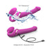 The Lovely Planet Strap-on-Me Multi Orgasm Bendable Strap-on with Clitoral Tongue - Large, is depicted in two positions: one with water splashing over it to emphasize its IPX 7 waterproof rating designed for clitoral stimulation, and another lying flat with an attached USB charging cable. The accompanying text highlights a 2-hour charge time and a 70-minute battery life.