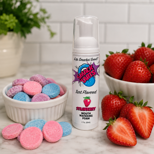 A bottle of SMACK Tarts Mouthwatering Sour Foam 2.7 oz stands beside fresh strawberries and bowls of pink, purple, and blue candy tablets on a countertop with a white tile background. Available in 6 flavors.