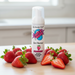 A can of SMACK Tarts Mouthwatering Sour Foam 2.7 oz stands on a wooden surface, surrounded by fresh strawberries in a bright kitchen. This tart-flavored, foaming oral lubricant is available in 6 flavors.