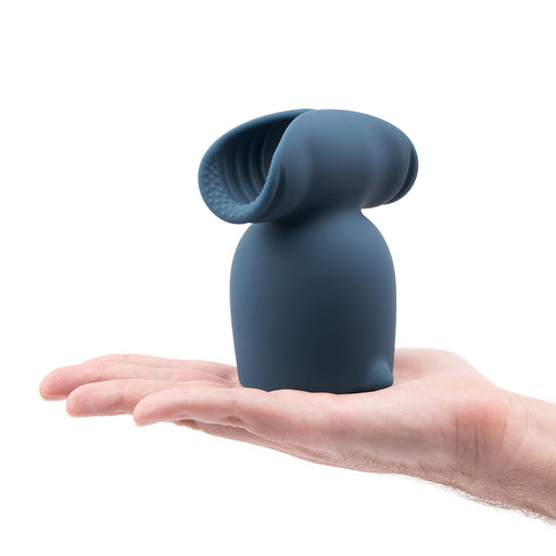 A hand holds the blue Stroke Silicone Penis Play Wand Attachment, featuring a rounded base and two curved, textured extensions at the top, against a white background.