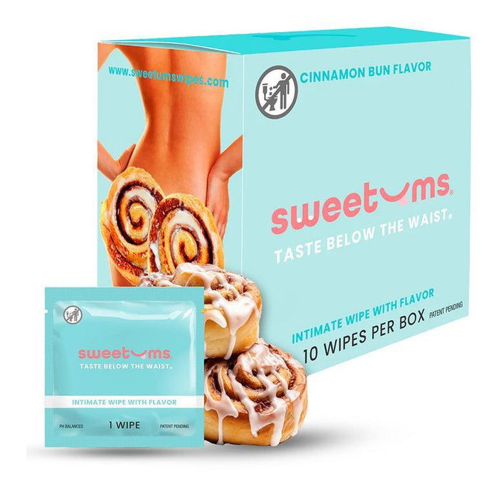A "Sweetums" box with cinnamon bun flavored wipes is displayed, showcasing a person from behind and cinnamon rolls. Made from plant fibers, these vegan, pH-balanced wipes are packaged with one packet and two cinnamon buns in front.