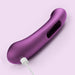 The Tempo G-Spot Tapping Pressure Sensing App-Controlled Vibrator, a purple curved toy with a handle opening, is shown charging via white USB cable on a light pink background, designed for targeted g-spot stimulation.