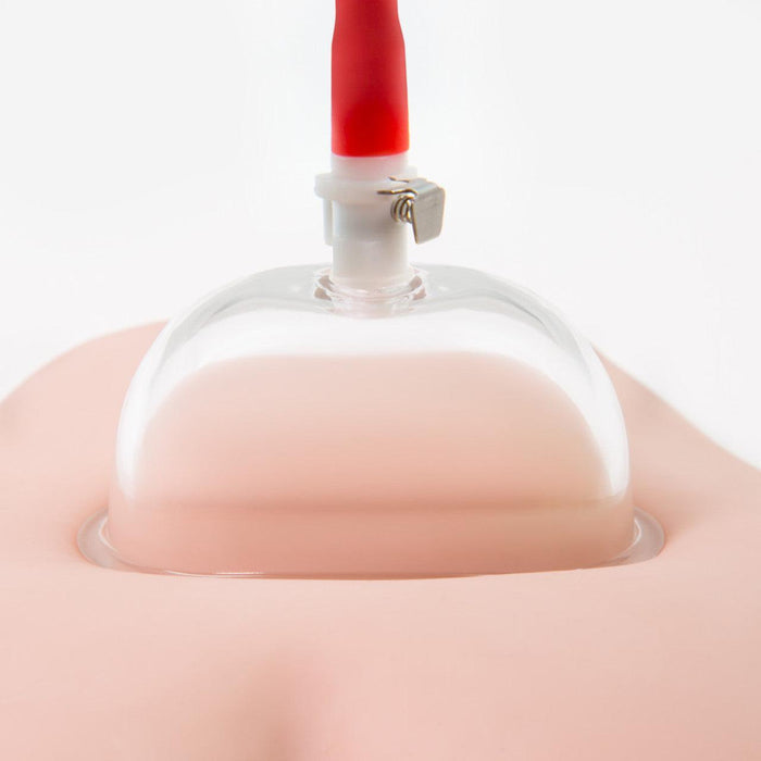 A close-up of the Temptasia Intense Pussy Pump System by Blush attached to a breast. The device features a transparent dome-shaped cup and a red and white valve connected to tubing at the top, similar to devices used for clitoris enhancement. The background is white, emphasizing the system's components.