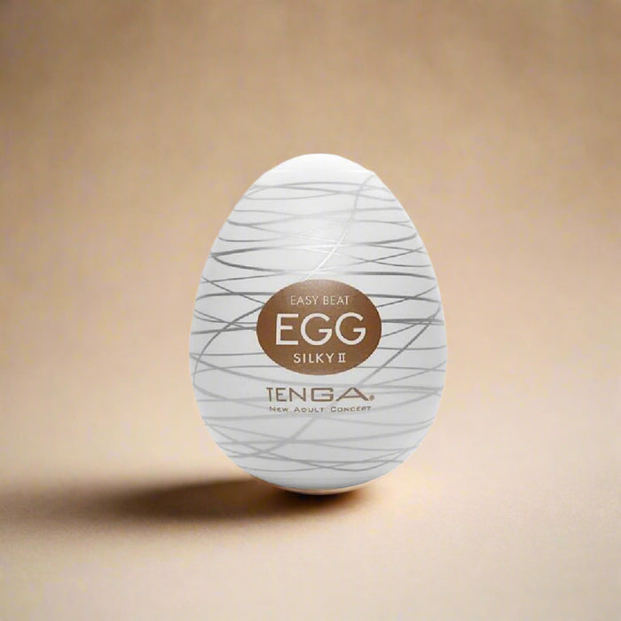 A white oval product with grey lines and a brown label reading "Tenga Egg Disposable Penis Masturbator - Silky 2" from Tenga, a New Adult Concept—your perfect travel buddy. This disposable masturbation sleeve is showcased against a plain white background.