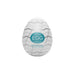 A Tenga Egg Disposable Penis Masturbator - Wavy 2, shown against a white background. The egg-shaped Tenga product is white with gray wave patterns and features a turquoise label in the center. Perfect as a travel buddy, this disposable masturbation sleeve ensures convenience on the go.