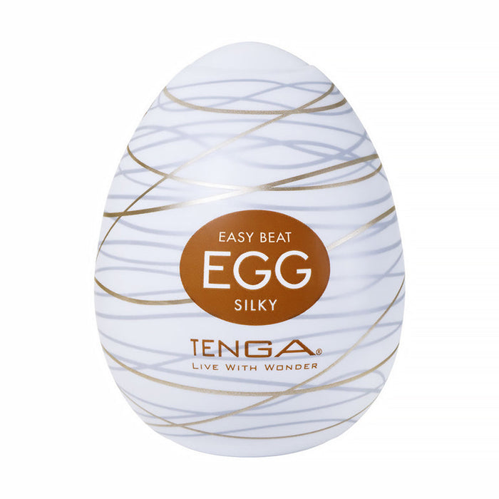 A discreet, white egg-shaped stroker with gold swirl patterns, labeled "Easy Beat Egg Silky." The Tenga Egg Standard 3 Pack Disposable Masturbators II features the TENGA brand and "Live With Wonder" slogan beneath the label.