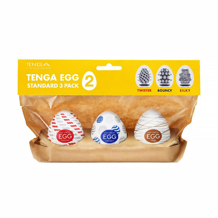 The Tenga Egg Standard 3 Pack Disposable Masturbators II includes three white egg-shaped pocket strokers with red, blue, and gold designs labeled "Twister," "Bouncy," and "Silky" on a yellow and brown holder.