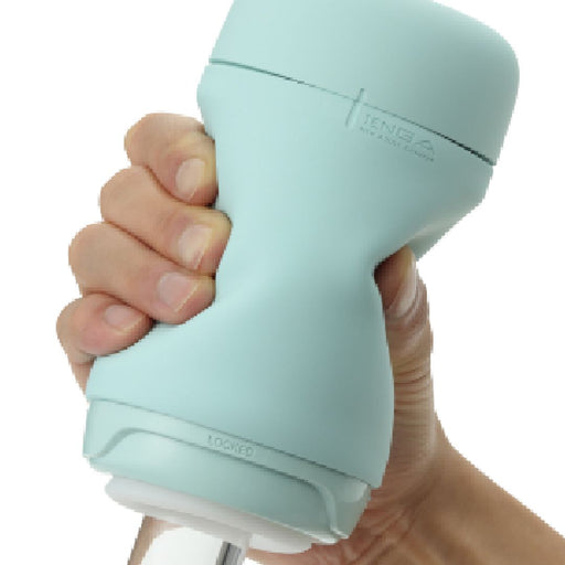 A hand holding a mint green Tenga Puffy Discreet Ultra Soft Beaded Masturbator with a cylindrical shape and silicone cover. The device features a twist mechanism for opening and locking, indicated by the text "LOCKED" near the base. The hand grips the device firmly, showcasing its ergonomic design that is easy to clean and maintain.