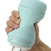 A hand holding a mint green Tenga Puffy Discreet Ultra Soft Beaded Masturbator with a cylindrical shape and silicone cover. The device features a twist mechanism for opening and locking, indicated by the text "LOCKED" near the base. The hand grips the device firmly, showcasing its ergonomic design that is easy to clean and maintain.