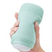 A hand holding a light green, ergonomically designed portable container labeled "Tenga" with a white base and an ultra-soft spongy material. The container appears to have a twist-lock mechanism. The product name is Tenga Puffy Discreet Ultra Soft Beaded Masturbator - Mint Green.