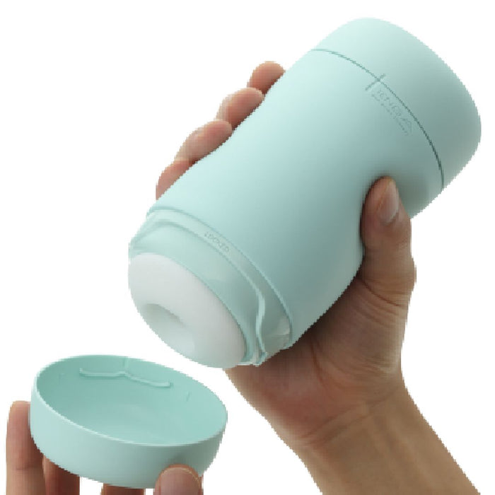 A hand is holding a cylindrical teal cup with a white interior. Another hand is removing the detachable lid from the bottom of the cup, which has a silicone cover for easy cleaning and maintenance. The Tenga Puffy Discreet Ultra Soft Beaded Masturbator - Mint Green and lid both have a smooth, matte finish.