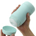 A hand is holding a cylindrical teal cup with a white interior. Another hand is removing the detachable lid from the bottom of the cup, which has a silicone cover for easy cleaning and maintenance. The Tenga Puffy Discreet Ultra Soft Beaded Masturbator - Mint Green and lid both have a smooth, matte finish.