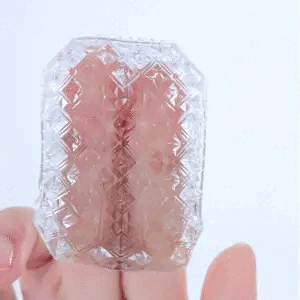 A hand holds a translucent, intricately carved crystal stone with pink tones, rotating it to display its detailed geometric patterns and sparkling facets against a plain white background.