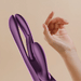 A close-up of a hand near the purple Terri App-Controlled G-Spot Tapping Rabbit Vibrator, featuring a curved silicone design for precise stimulation, set against a neutral beige background.
