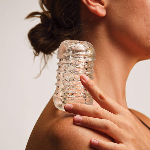 A person holds The Handy Dream Collection Touch Sleeve, a small clear textured glass object, with a realistic hand-like grip against their bare shoulder; only the lower face and neck are visible.