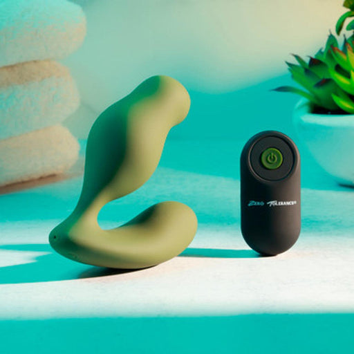 The Sergeant Powerful Prostate Vibrator with Remote Control by Evolved Novelties is showcased here in green, accompanied by its black remote control, both elegantly arranged on a light surface. In the background, neatly stacked white towels and a small succulent plant in a white pot create a serene ambiance under soft lighting. This waterproof and submersible prostate vibrator offers 10 vibrating speeds for an enhanced experience.