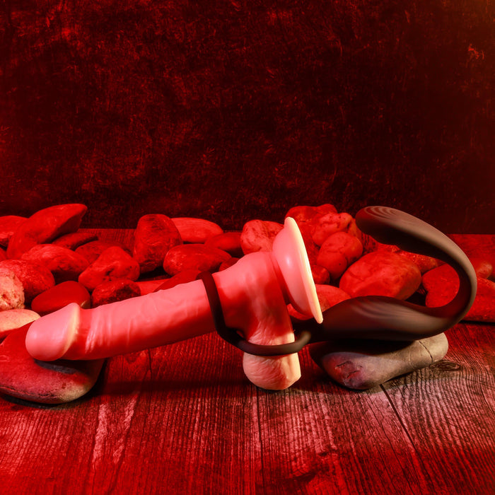 A scene on a wooden surface with red lighting features The Wrangler Vibrating Cock Ring and Butt Plug with Remote by Evolved Novelties, accompanied by smooth stones. The erotic atmosphere is amplified by the striking red and black color scheme.