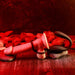 A scene on a wooden surface with red lighting features The Wrangler Vibrating Cock Ring and Butt Plug with Remote by Evolved Novelties, accompanied by smooth stones. The erotic atmosphere is amplified by the striking red and black color scheme.