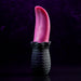 A black, textured base holding a realistic red tongue-like object stands vertically against a dark purple background. The Tongue Teaser Flickering Realistic Red Tongue Vibrator by Evolved Novelties offers lifelike oral sensations, combining the detailed ridged base with the smooth, glossy appearance of the red tongue shape.