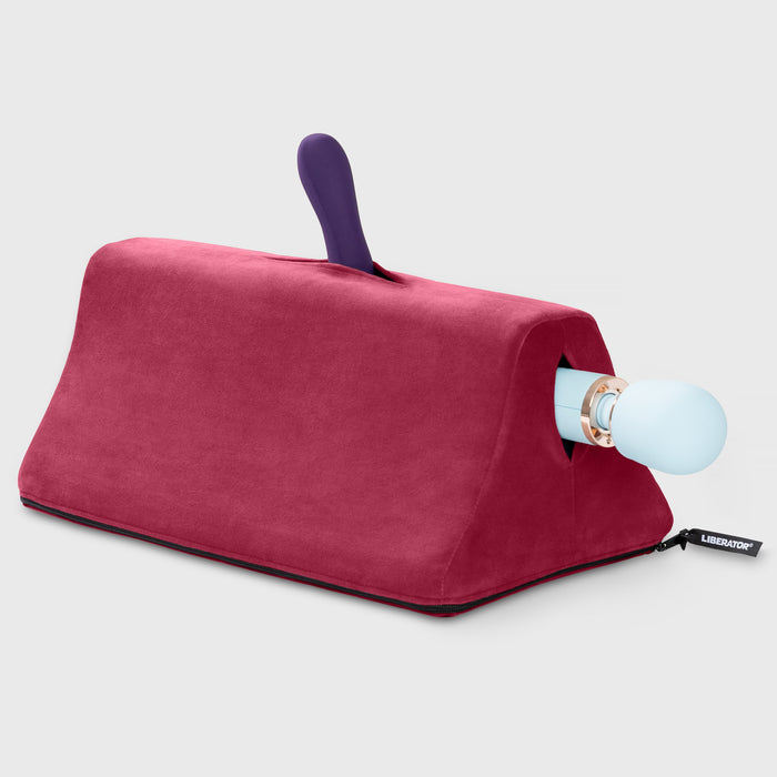 The Liberator Tula – Dual-Toy Sex Cushion for Double the Pleasure is a maroon triangular foam wedge with a zippered opening, holding one purple upright and one light blue horizontal vibrator securely for ergonomic enjoyment.