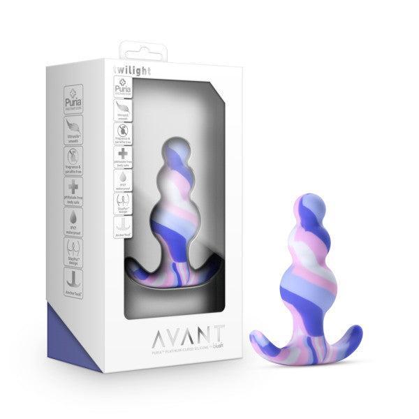 A white box with a clear window showcases the Twilight Beginner Purple and Pink Silicone Butt Plug by Blush, featuring a vibrant gradient design in shades of purple, blue, and pink. The packaging is adorned with various icons and text that highlight its premium platinum-cured silicone material, making it ideal for anal beginners.