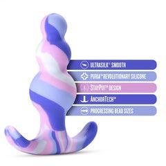 The Twilight Beginner Purple and Pink Silicone Butt Plug by Blush is perfect for anal beginners, featuring pastel tones and a wavy, textured surface. This premium platinum-cured silicone plug offers "UltraSilk Smooth," "Puria Revolutionary Silicone," "StayPut Design," "AnchorTech," and "Progressing Bead Sizes," all highlighted in stylish blue and purple text boxes.