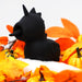 Among bright orange leaves and mini pumpkins sits the Unihorn Wild Spirit Vibrator with LickingTongue by Creative Conceptions, a sleek, silicone dark pleasure companion shaped like a black unicorn. The whimsical Halloween-themed scene features this unique product with its distinctive horn, small tuft of hair-like texture, and closed eyes.
