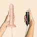 A hand holds the Strap-On-Me Realistic 7.5 Inch Silicone Squirting Dildo - Vanilla with an attached tube, while another hand holds a black handheld pump connected by the tube, against a light peach background.