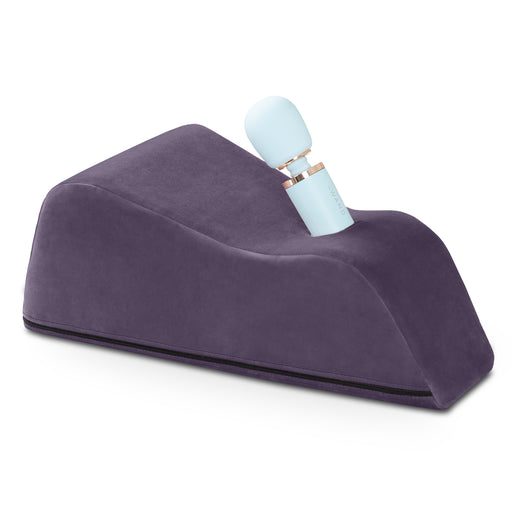 The Liberator Wanda – Hands-Free Wand Mount is a wedge-shaped, dark purple cushion with a slot on top for a light blue Magic Wand massager, offering soft, ergonomic support for hands-free enjoyment.