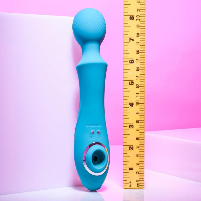 The Evolved Novelties Wanderful Sucker Double Ended Wand + Clitoral Pulsation Vibrator in electric blue is displayed standing beside a yellow ruler for size reference. The ruler shows that the silicone massager measures approximately 10 inches long. The backdrop features a gradient of soft pink and white tones.