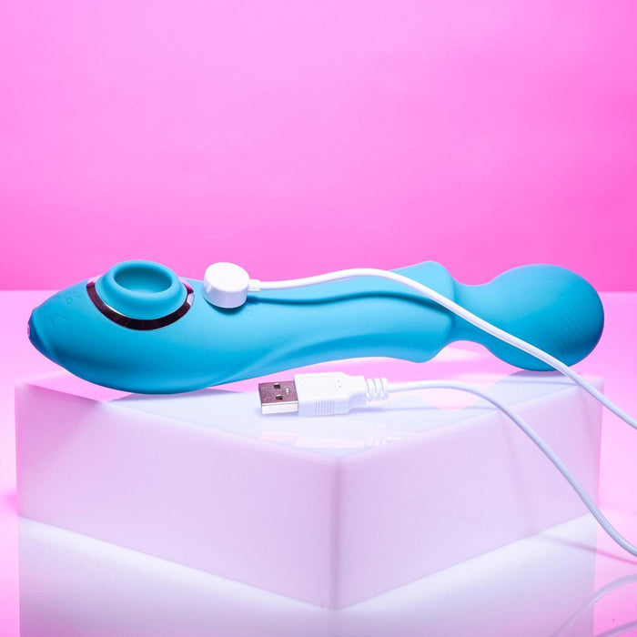 The Wanderful Sucker Double Ended Wand + Clitoral Pulsation Vibrator from Evolved Novelties, featuring a unique curved design and vibrant blue silicone finish, lies on a white surface against a pink background. The device is connected to an included white USB charging cable, which is also visible in the image.