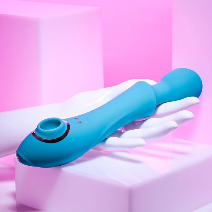 The Wanderful Sucker Double Ended Wand + Clitoral Pulsation Vibrator - Blue by Evolved Novelties, featuring a rounded silicone head and control buttons, is displayed on a white mannequin hand against a pink background with white geometric shapes.