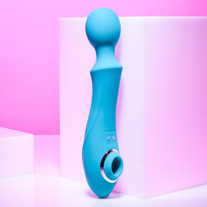 The Wanderful Sucker Double Ended Wand + Clitoral Pulsation Vibrator by Evolved Novelties, in a stunning blue color, with a rounded silicone head and ergonomic handle, is showcased against a pink and white backdrop. The device boasts a modern, sleek design featuring clearly visible buttons and circular accents near the base.