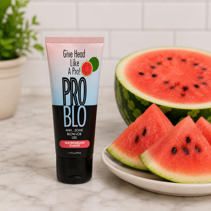 A tube of Pro Blo Oral Pleasure Gel 1.5 oz stands beside a plate of watermelon slices and a halved melon, featuring playful text and watermelon imagery. The gel is available in 8 flavors.