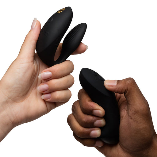 Two hands hold the We-Vibe Chorus Pro Wearable Couples' Vibrator with Triple Motors & Remote; the left displays the curved, dual-ended vibrator for G-spot stimulation, while the right holds its remote, against a white background.