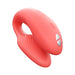 The We-Vibe Chorus Remote & App Controlled Couples' Vibrator in Coral is a pink, curved silicone couples toy with an adjustable fit, smooth finish, ribbed inner surface, and two silver buttons, shown on a white background.